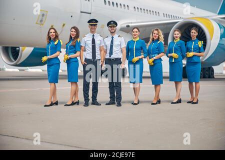 Beaux pilotes et belles hôtesses debout à l'extérieur dans l'aérodrome Banque D'Images