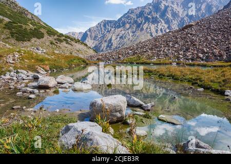 Paysage d'été idyllique avec sentier de randonnée dans les montagnes avec de beaux pâturages de montagne vert frais, rivière avec reflet et nuages. Banque D'Images