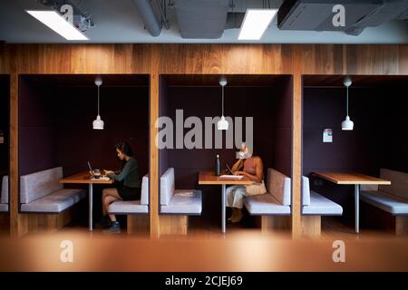 Femmes d'affaires travaillant dans des cabines socialement distancées dans le bureau moderne pendant Pandémie de santé Banque D'Images