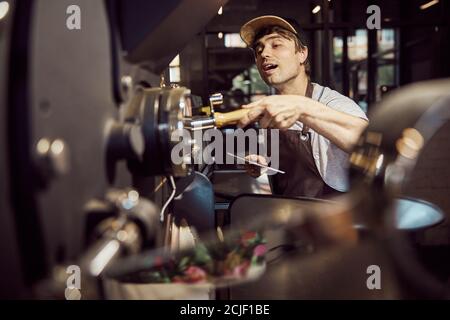 Beau travailleur masculin contrôlant le travail de la machine à rôtir à café Banque D'Images
