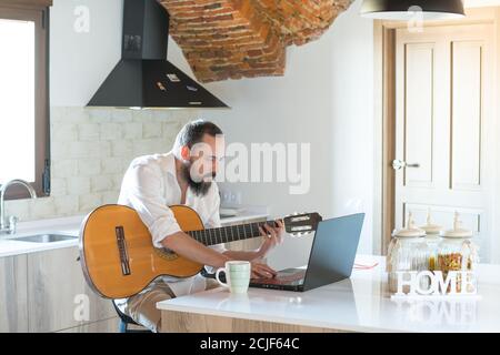 hipster gars avec une barbe prenant des leçons de guitare avec son ordinateur portable Banque D'Images