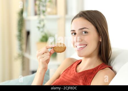 Bonne femme tenant un cookie de céréales vous regardant assis sur un canapé dans le salon à la maison Banque D'Images