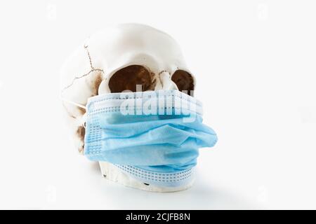 Crâne humain portant un masque chirurgical bleu sur fond blanc, vue latérale Banque D'Images