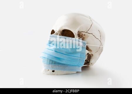 Crâne humain portant un masque chirurgical bleu sur fond blanc, vue latérale Banque D'Images