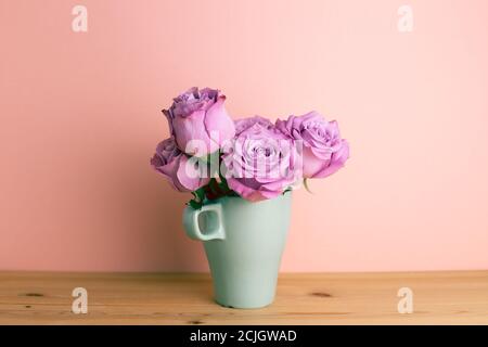 Fleurs roses violettes dans une tasse en céramique sur une table en bois avec fond rose. Arrangement floral, espace de copie Banque D'Images