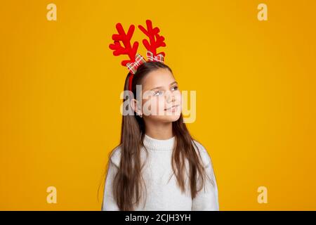 Enfant attendant le Père Noël. Belle petite fille avec des cornes dans le chandail regarde vers le haut à l'espace vide Banque D'Images