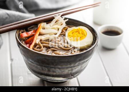 Soupe asiatique de nouilles avec nouilles soba, légumes et œufs dans un bol sur table blanche. Banque D'Images