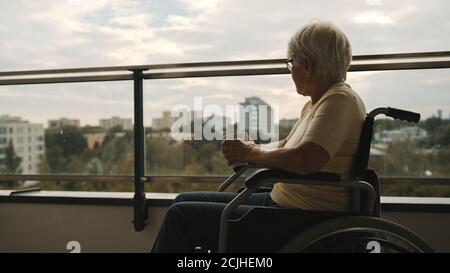 une vieille femme handicapée en fauteuil roulant sur la terrasse buvant une tasse de thé ou de café. . Photo de haute qualité Banque D'Images