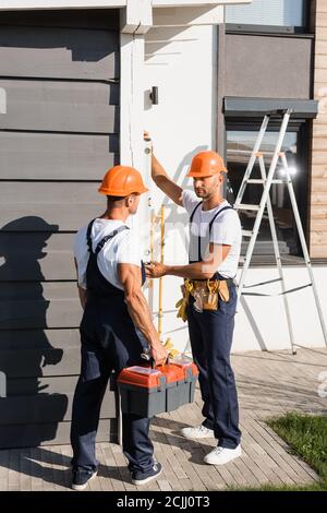 Constructeur dans la boîte à outils de maintien des uniformes près d'un collègue avec niveau à bulle et bâtiment Banque D'Images