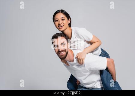 homme barbu en t-shirt blanc coggyendant excitée petite amie asiatique isolée en gris Banque D'Images