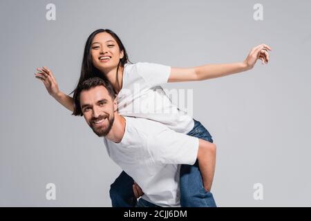 jeune homme en t-shirt blanc piggyendant excitée de petite amie asiatique imitant voler isolé sur gris Banque D'Images