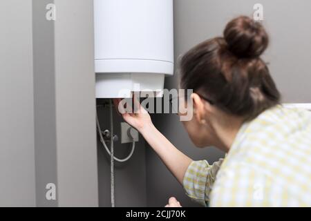 Chauffe-eau domestique, femme règle la température sur un chauffe-eau électrique Banque D'Images