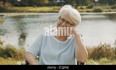 Vieille femme pensive dans le fauteuil roulant assis près de la rivière . Photo de haute qualité Banque D'Images
