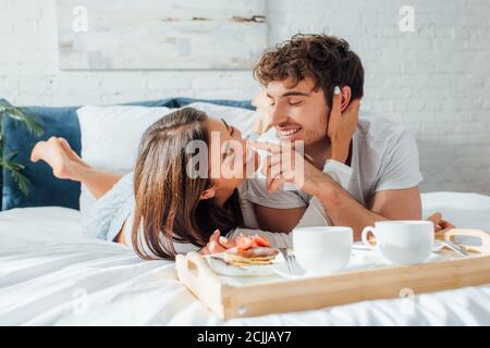 Foyer sélectif des jeunes couples se touchant près du café et crêpes sur le plateau de petit déjeuner sur le lit Banque D'Images