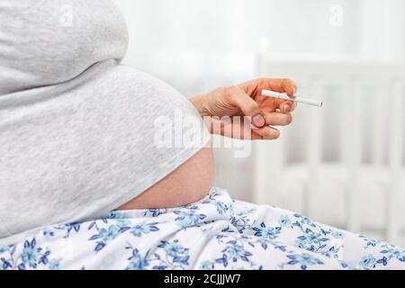 Une femme enceinte avec une cigarette dans les mains. Main avec une cigarette et l'estomac gros plan. Le concept de dépendance à la nicotine et de préjudice à la grossesse. Banque D'Images