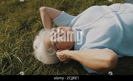 Grand-mère cool, femme avec des écouteurs couchés sur l'herbe et écoutant la musique. Photo de haute qualité Banque D'Images
