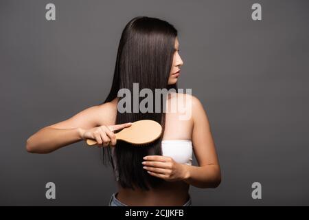 vue rognée de la femme brunette se brossant les cheveux brillants isolée sur noir Banque D'Images