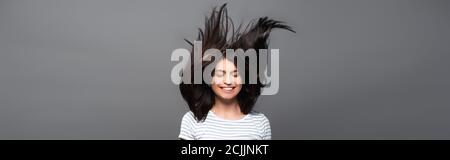 brunette femme aux cheveux longs sautant et souriant isolée sur une photo panoramique noire Banque D'Images