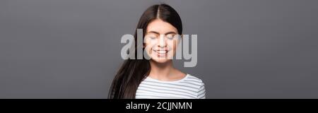 brunette femme aux cheveux longs avec les yeux fermés souriant isolée sur une photo panoramique noire Banque D'Images