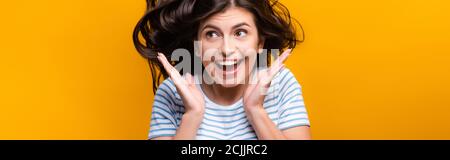 brunette femme aux cheveux longs avec des boucles sautant et souriant isolée sur jaune, photo panoramique Banque D'Images