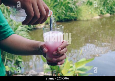 Un homme verse un soda dans un verre de lait et de sirop rouge pour faire du soda laiteux rose ou du soda Gembira. Banque D'Images