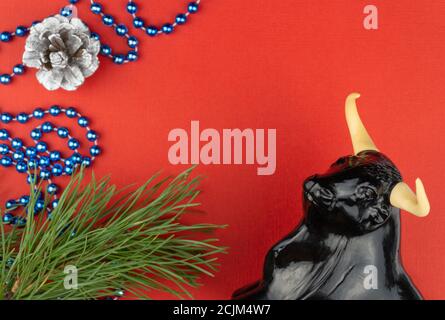 Statuette d'un taureau sur fond rouge de Noël. Mise au point sélective. Décorations de fête et branches de sapin avec cônes. Banque D'Images