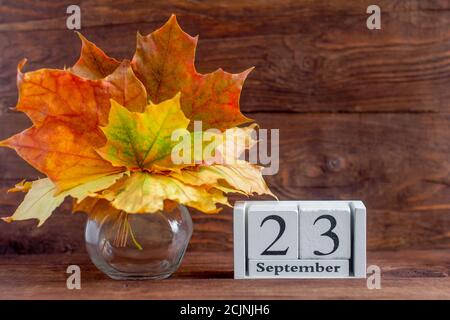 Septembre 23 sur un calendrier en bois et un bouquet d'automne de feuilles de couleur érable. Date du mois d'automne. Le concept de l'automne doré. Banque D'Images