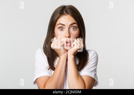 Gros plan de jeune fille intriguée, penchée sur les mains et regardant demandé à la caméra, haletant impressionné, fond blanc Banque D'Images