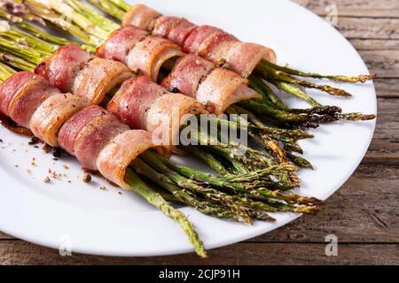 Asperges vertes enveloppées de bacon sur une table en bois. Banque D'Images