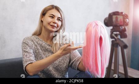 Femme blogger enregistre la vidéo. Elle parle de coupes de cheveux et montre une perruque rose. Styliste et consultant en mode enregistrant la conférence Banque D'Images