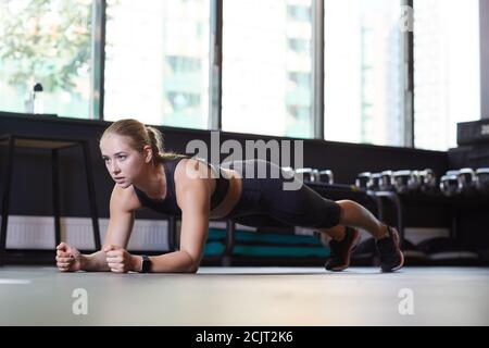 Jeune femme mince dans des vêtements de sport faisant pousser-UPS sur le étage dans la salle de sport Banque D'Images