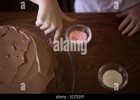 Un jeune enfant qui se laque un doigt dans la glaçage au chocolat Un gâteau d'anniversaire Banque D'Images