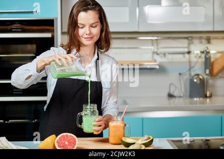 jolie femme versant un jus de détox vert du blender à un verre, à la maison portant des vêtements décontractés. photo de gros plan Banque D'Images