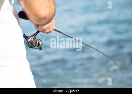 Gros plan les mains des pêcheurs qui s'enroulent dans le rabatteur au bord de la mer. Les mains du pêcheur, tient la tige de rotation, fait tourner la poignée de l'antenne. Passe-temps et Banque D'Images