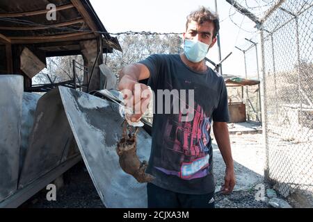 Un homme tient dans ses mains une souris sauvage qui a été brûlée pendant les flammes flamboyantes.des milliers de personnes ont été forcées de fuir leur maison après qu'un incendie a éclaté dans le camp de Moria détruisant leurs maisons et leurs biens. Banque D'Images