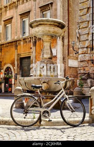 Vieux vélo à côté d'une fontaine sur une petite place Entouré de vieux bâtiments dans le centre de Rome Banque D'Images