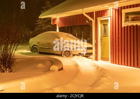 Voiture de couleur argent recouverte de neige beaucoup plus fraîche chute de neige. Le parking se trouve à proximité d'un garage en bois rouge, dans un style typiquement suédois. Nuit, Banque D'Images