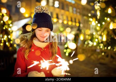 Jolie jeune fille tenant des scincheurs près d'un arbre de Noël sur la foire traditionnelle de Noël à Riga, Lettonie. Les enfants fêtent le nouvel an. L'hiver, c'est bien