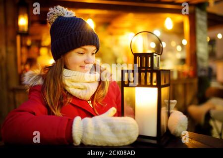 Jolie jeune fille regardant une lanterne sur la foire traditionnelle de Noël à Riga, Lettonie. Les enfants apprécient les bonbons, les bonbons et le pain d'épice sur le marché de Noël. Banque D'Images