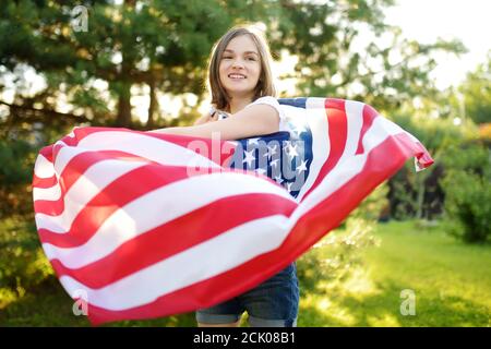 Jolie jeune fille portant un drapeau américain à l'extérieur le beau jour d'été. Concept de jour de l'indépendance. Enfant célébrant la fête nationale. Jour du souvenir. Banque D'Images