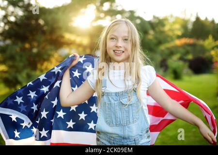 Jolie jeune fille portant un drapeau américain à l'extérieur le beau jour d'été. Concept de jour de l'indépendance. Enfant célébrant la fête nationale. Jour du souvenir. Banque D'Images