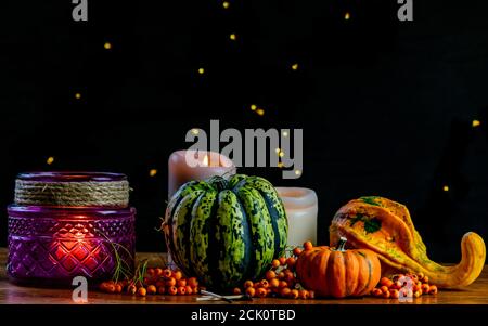 Variété de citrouilles, de baies de rowan et de bougies sur table en bois rustique et fond noir avec bokeh. Automne légumes symboliques en vert, jaune et Banque D'Images