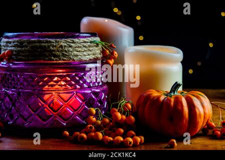 Lanterne violette, citrouille dorée orange baies rowan et deux bougies sur table rustique en bois et fond noir avec points de bokeh jaunes Banque D'Images