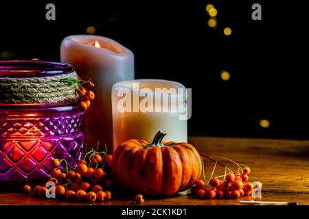 Lanterne violette, citrouille dorée orange baies rowan et deux bougies sur table rustique en bois et fond noir avec points de bokeh jaunes Banque D'Images