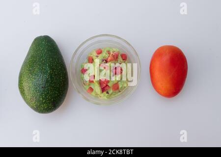 Vue de dessus de la sauce guacamole dans un pot en verre avec un avocat entier et une tomate Banque D'Images