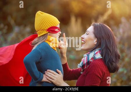 Bonne famille à l'automne ! Mère et fille marchant dans le parc et appréciant la belle nature d'automne. Enfant fille joue super-héros. Banque D'Images