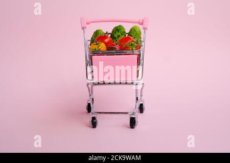 Chariot d'épicerie rose plein de tomates et de concombres sur rose arrière-plan Banque D'Images