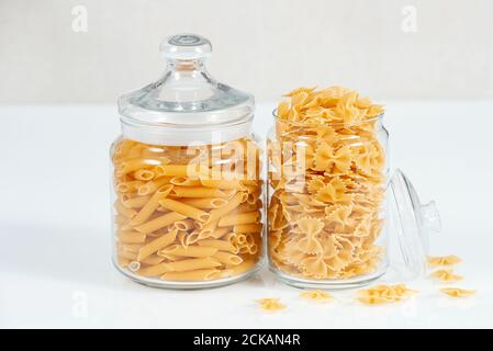 Divers types de pâtes brutes sur fond blanc. Pots en verre avec différents types de pâtes, spaghetti et nouilles. Banque D'Images