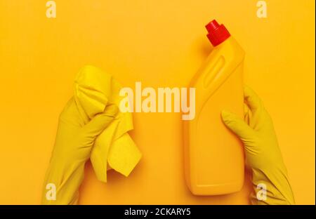 mains dans des gants jaunes tenir un chiffon jaune et une bouteille jaune de liquide de toilette sur un fond jaune. place pour le texte. Banque D'Images