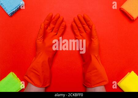mains dans des gants en caoutchouc orange au centre autour d'un chiffon sur fond rouge. Banque D'Images